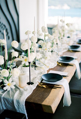 White bouquets of flowers stand on a narrow canvas on a festive table next to black plates on napkins