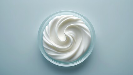 Whipped cream swirls in a clear bowl on a light blue background, showcasing a delicious dessert topping