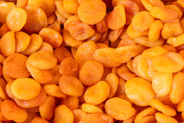 Close-up of dried apricots creating a seamless textured pattern with variations in color and translucency where soft curved shapes overlap forming a natural fruit background