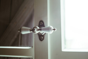 Close-up of a porcelain door handle with an oblong shape, attached to a dark wood door, near a brightly lit window.
