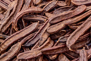 Background of dried carob pods with wrinkled dark brown surfaces elongated shapes create a natural texture