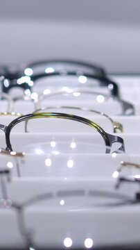 Vertical screen, multiple eyeglasses are neatly arranged and displayed on a bright white shelf, showcasing a variety of styles and designs for customers to browse and choose from in an optical store