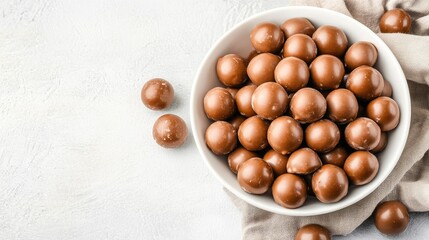 Obraz premium Chocolate-covered maltesers are thoughtfully placed in a white bowl set on a grey surface, offering a minimalist aesthetic