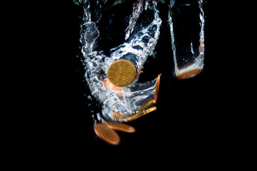 Euro cent coins fall with a splash into  water on black background