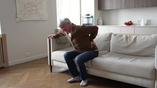 Anguished haggard tortured senior man grimacing, clutching lower back in agony. Cant walk, herniated disc nerve compression, chronic spinal disorder, unbearable backache, degenerative spine disease