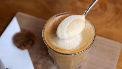 Professional barista carefully removing excess milk foam from layered latte macchiato, creating perfectly crafted coffee beverage with precise culinary skill. Thick cappuccino foam in a spoon