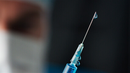Close Up Of Male Member Of Medical Team In Hospital Wearing Mask With Syringe Preparing Injection