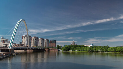 Obraz premium Bridge over Ishim with park timelapse with the transport and clouds on the background. Central Asia, Kazakhstan, Astana