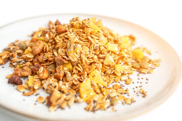 A bowl of granola with nuts and seeds on a white plate. The granola is a mix of different types of grains and nuts, and it looks like a healthy snack.