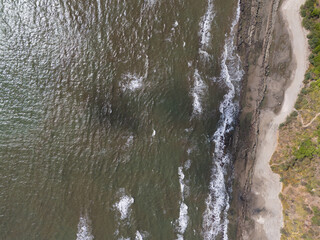 Waves crashing on rugged coastline with sandy beach under clear sky