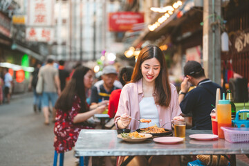 Young adult traveler woman enjoy eating street food spicy thai tasty menu travel at chinatown Yaowarat, Bangkok, Thailand