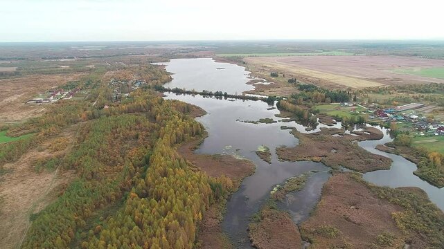Large body of water with trees and a town in the background. The water is brown and murky. Autumn colors of nature, the source of a forest stream and a small village on the edge of the lake.