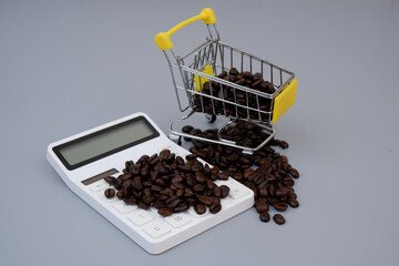 Coffee price concept. Coffee beans on calculator and shopping cart on gray background.