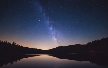 A night sky with stars and a reflection on a dark lake.