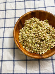 Sprouted green buckwheat in a wooden bowl close-up on a white tablecloth in a blue checkered pattern