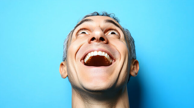 A close-up shot of a man's face, head tilted back, showcasing a wide, joyful, open-mouthed laugh against a vibrant blue background.  The image conveys happiness, exuberance, and positive emotions.