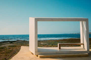 Paphos waterfront, Cyprus. A cubic white bench with modern architecture set against the deep blue Mediterranean Sea. A concept of paradise vacation, Mediterranean landscapes of Cyprus and Greece