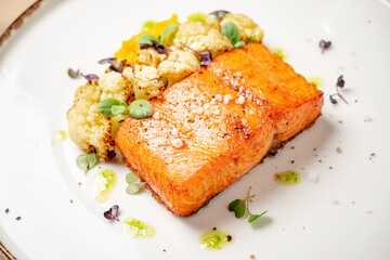 Exquisite salmon fillet is elegantly plated with roasted cauliflower and colorful microgreens