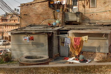 Two Nepalese women sat outside a corrugated iron shack under some washing