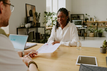 African American candidate in smart clothes giving her resume and cover letter to unrecognizable...