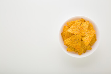 Full white bowl of yellow tortilla chips on light gray table background. Closeup. Empty place for text. Top down view.