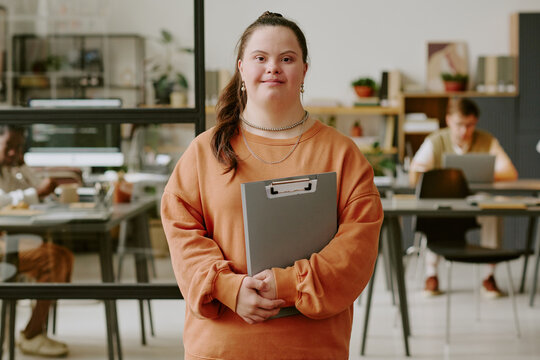 Portrait of smiling female office worker standing in office and holding gray clipboard