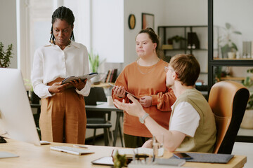 Fototapeta premium Wide shot of unrecognizable man at computer chair having lively discussion with his biracial colleague who looking at presentation on screen
