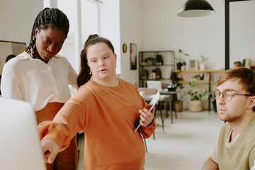 Medium shot of valued employee with tablet in hand pointing at computers display while...