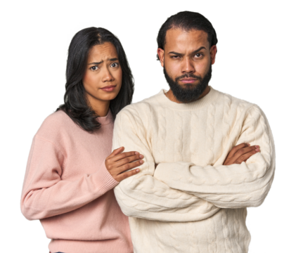 Young Latino couple in studio unhappy looking in camera with sarcastic expression.