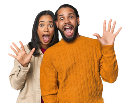 Young Latino couple in studio receiving a pleasant surprise, excited and raising hands.