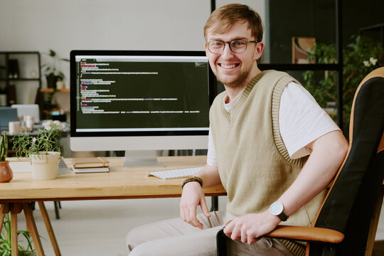 Portrait of smiling and confident young man sitting in chair posing for photo while spending work day in office