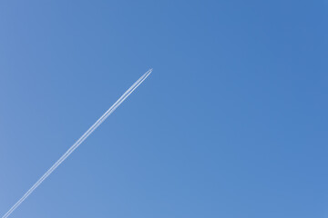 Airplane in a blue sky without clouds. The airplane has a flight trail behind it