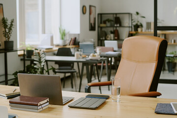 Wooden desk with laptop and office supplies on top and beige leather computer chair in modern office