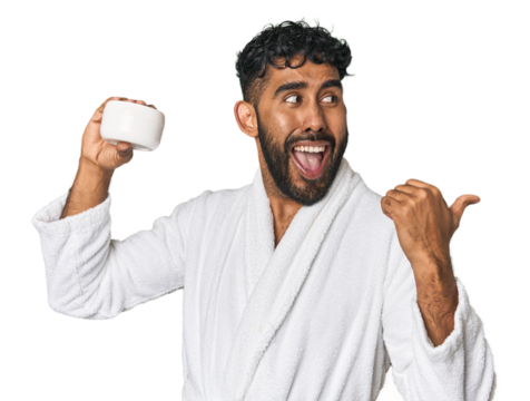 Hispanic male with moisturizer in studio points with thumb finger away, laughing and carefree.