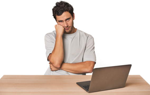 Hispanic young man working on laptop who feels sad and pensive, looking at copy space.