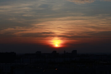 The sun goes behind the clouds on the horizon above the city. The sun is immersed in the clouds on the horizon.