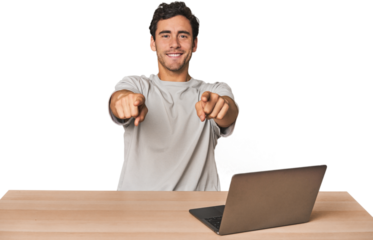 Hispanic young man working on laptop cheerful smiles pointing to front.