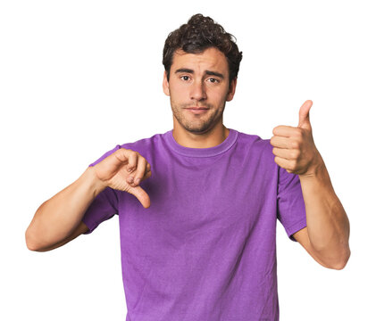 Young Hispanic man in studio showing thumbs up and thumbs down, difficult choose concept