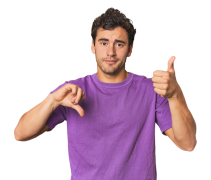 Young Hispanic man in studio showing thumbs up and thumbs down, difficult choose concept