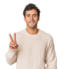 Naklejka premium Young Hispanic man in studio showing victory sign and smiling broadly.