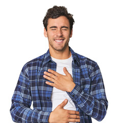 Young Hispanic man in studio laughs happily and has fun keeping hands on stomach.