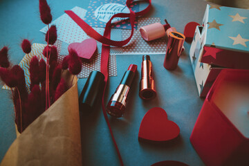 Lipsticks, nail polish, langurus and red hearts on dark paper background. Valentine's day