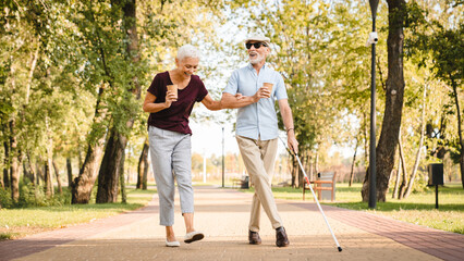 Obraz premium Elderly couple walking in the park talking laughing . Senior man is blind and senior woman helping him to walk. Senior couple spending time in nature. Couple enjoying outdoors retirement.