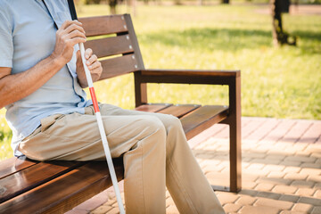 Side view visually impaired blind senior man holding white and red guide cane walking stick,...