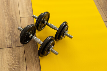 Two cast iron dumbbells and a yellow fitness mat. Natural. Playing sports at home