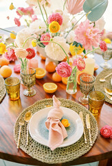 Knotted napkin lies on a plate on a wicker rug on a festive table in front of a colorful bouquet of flowers