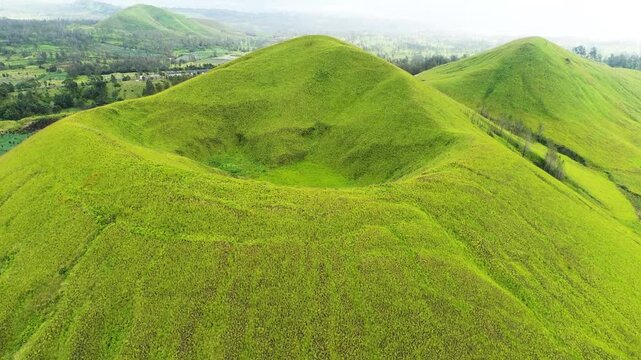 aerial view of green hills peak with grassland and mountain views of Wurung Crater, Indonesia. Aerial shot of the green grassy peak of the mountain crater.