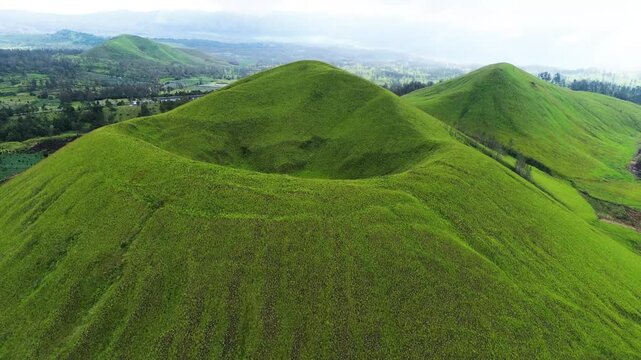 aerial view of green hills peak with grassland and mountain views of Wurung Crater, Indonesia. Aerial shot of the green grassy peak of the mountain crater.
