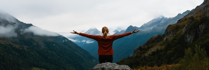 A person stands atop a mountain embracing the beauty of nature with arms wide open, symbolizing...