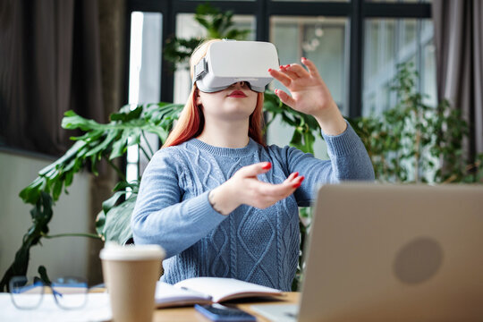 Young business woman at office wearing vr headset work with laptop iInteracting with AR technology. Virtual reality technology. Workplace with greens. Future technology concept. - Powered by Adobe